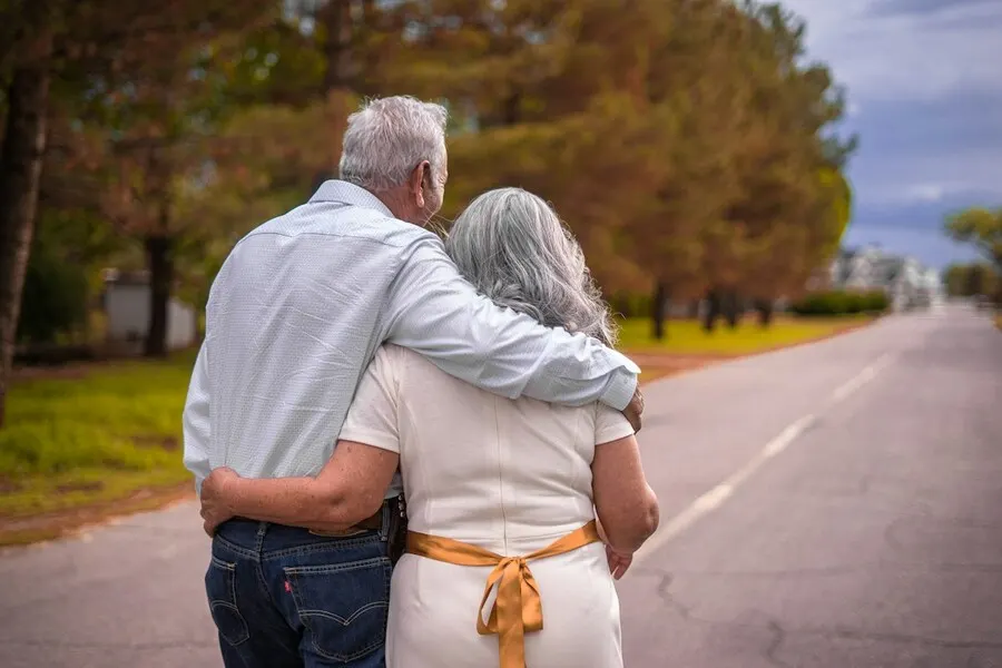Older couple with gray hair walking arm in arm down a country road